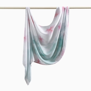 Detail eines weißen Schleier-Schals mit rosa Blumendrucken am hölzernen Kleiderbügel