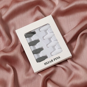 Detailaufnahme von 8-teiligen Kunststoff Hijab Nadeln in Grau und Weiß auf rosa Satin Stoff.