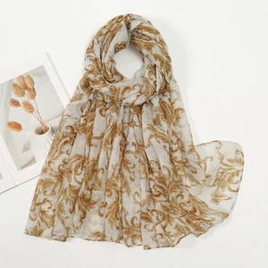 Dettaglio di sciarpa in voile con motivi floreali barocchi dorati su tessuto beige chiaro
