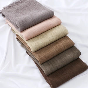 Close-up of stacked earth-toned scarves with delicate fringed edges and pleated fabric texture