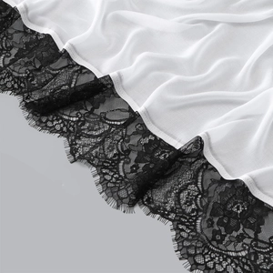 Detailed view of lightweight white fabric with delicate black eyelash lace floral trim