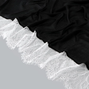Close-up of black fabric with delicate white floral eyelash lace trim on the hem