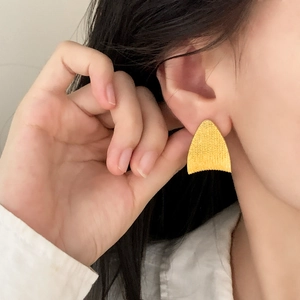 Chic gold fan-shaped stud earrings with brushed metal texture worn on a model