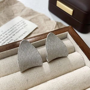 Macro shot of silver-toned triangle earrings with granular texture on velvet display