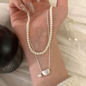 Elegant double-layered necklace with white pearls and matte metallic pebble pendant on hand