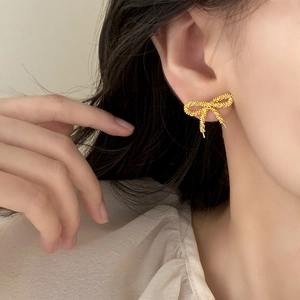 Elegant gold bow earrings with irregular textured surface worn by a model in close-up