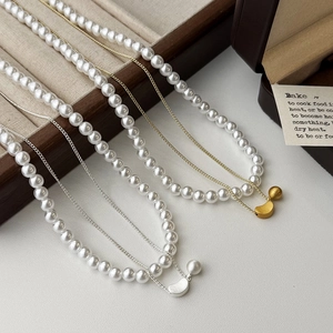 Close-up of double-layer pearl necklace with metallic crescent pendant on jewelry tray