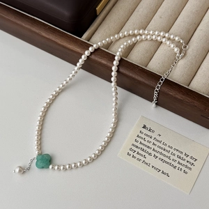 Detail of a pearl necklace with a green four-leaf clover pendant on a jewelry tray