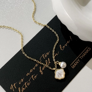 Collier élégant doré avec perle blanche et pendentif coquille irisée sur carte noire