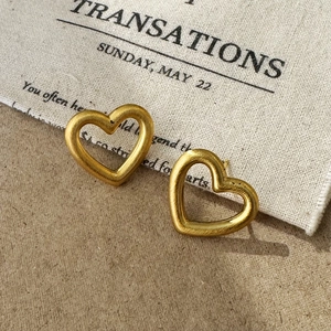 Close-up of matte champagne gold hollow heart stud earrings with brushed metal texture