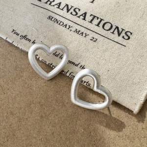 Macro shot of matte silver heart-shaped stud earrings with a brushed metallic texture