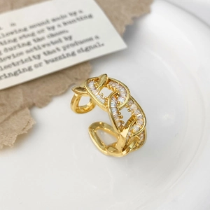 Detail eines Goldkettenrings mit klaren Zirkonen auf weißem Teller und Kraftpapierhintergrund