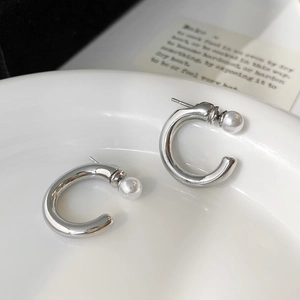 Gros plan de boucles d'oreilles C en argent avec perles blanches sur plat blanc
