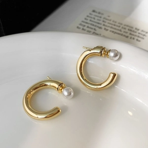Macro de boucles d'oreilles créoles dorées en C avec perles sur un plateau en céramique