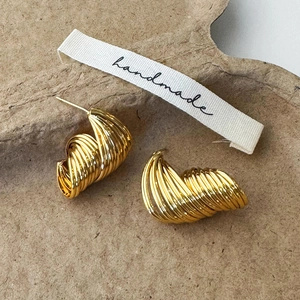 Detailed close-up of golden spiral stud earrings on a textured brown paper tray