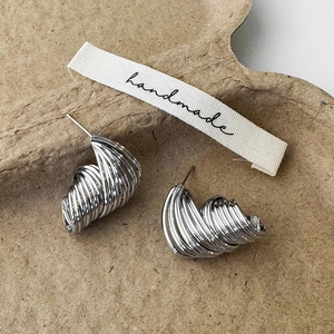 Macro shot of silver textured spiral stud earrings resting on a handmade craft paper tray