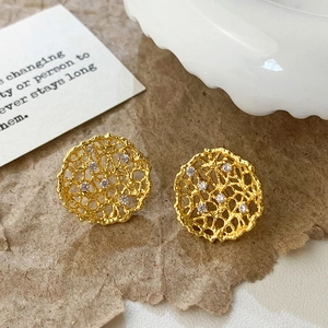 Macro shot of gold-plated hollow mesh earrings with micro-inlaid zircons on textured paper