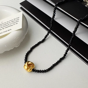 Gros plan du collier de perles facettées noires avec pendentif noeud torsadé doré