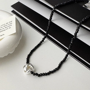 Vue macro du collier en perles noires avec un pendentif noeud tressé en argent poli