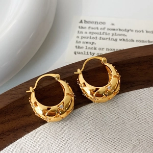 Détail de boucles d'oreilles cœur dorées avec zircons sur un support rustique chic