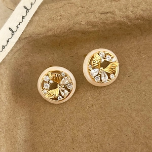 Macro view of gold butterfly zircon earrings with creamy resin ring on brown paper