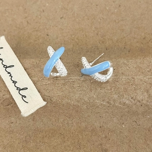 Macro detail of X-shaped cross earrings with light blue enamel and sparkling zircon