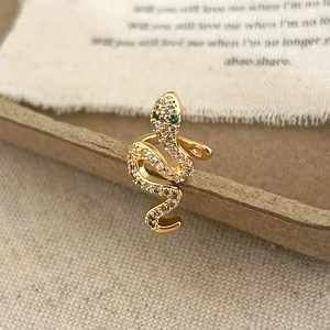 Detailed view of a gold snake ear cuff with white zircons and green gemstone eyes