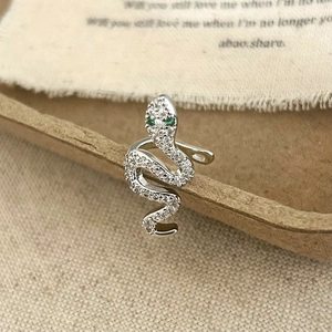 Macro view of silver snake ear cuff with white zircons and green gemstone eyes