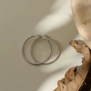 Close-up of large silver hoop earrings with pave-set crystals on a natural stone background