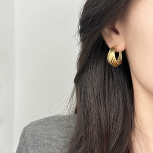 Elegant gold-tone multi-layered textured hoop earrings worn by a model in a side profile