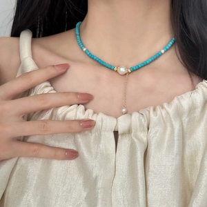 Blue turquoise bead necklace with white pearls and gold tassel pendant worn by a model