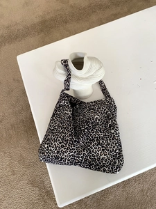 High-angle shot of a leopard print corduroy hobo bag on a white sculptural vase
