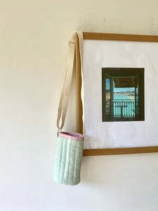 Dettaglio borsa termica trapuntata verde chiaro con bordo rosa su cornice in legno