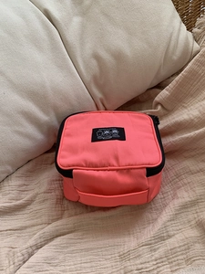 Detail of a bright pink nylon portable makeup bag featuring a black zipper and handle