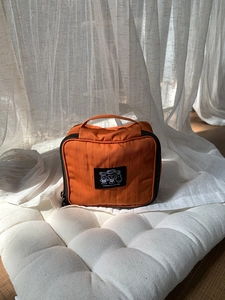 Detail of an orange nylon toiletry bag featuring a cute cartoon bear and sturdy top handle