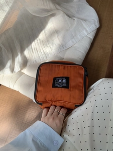 Detail of the compact orange nylon travel toiletry bag with hand carry strap and logo