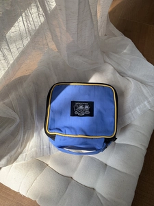Close-up of blue nylon makeup bag with yellow piping and cartoon label detail