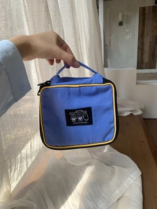 Blue nylon makeup bag with yellow trim and cartoon patch, shown in handheld view