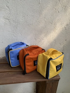 Detail showing various colors of nylon travel makeup bags with sturdy handles on a bench
