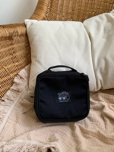 Detail of black nylon travel cosmetic bag with cartoon animal patch on woven chair