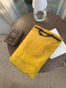 Close-up of ginger yellow travel storage bag with brown zipper and woven handle detail