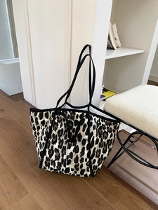 Detail of leopard print quilted tote bag with black canvas straps on wooden floor