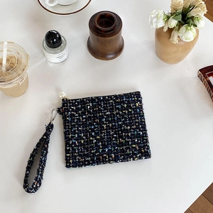 Mini tweed make-uptasje met gouddraad en parelrits op een wit bureau