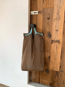 Brown nylon travel packing cube with blue handles hanging on a black doorknob for storage