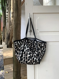 Quilted leopard print tote bag with black strap hanging on door in natural light setting