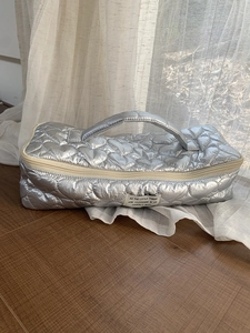 Detail of silver heart-quilted storage bag featuring a top handle and woven label