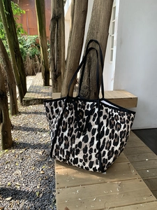 Detail of quilted leopard print tote bag on a sunlit wooden bench in a garden setting