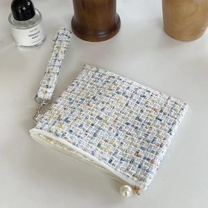 Detail van kleurrijke tweed make-uptas met witte ritssluiting en een parelhanger