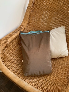 Detail of ultralight brown travel organizer with blue zipper and handle on rattan chair