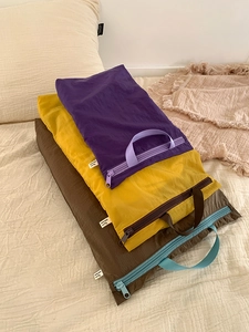 Three travel storage bags in purple yellow and brown stacked on a soft bed